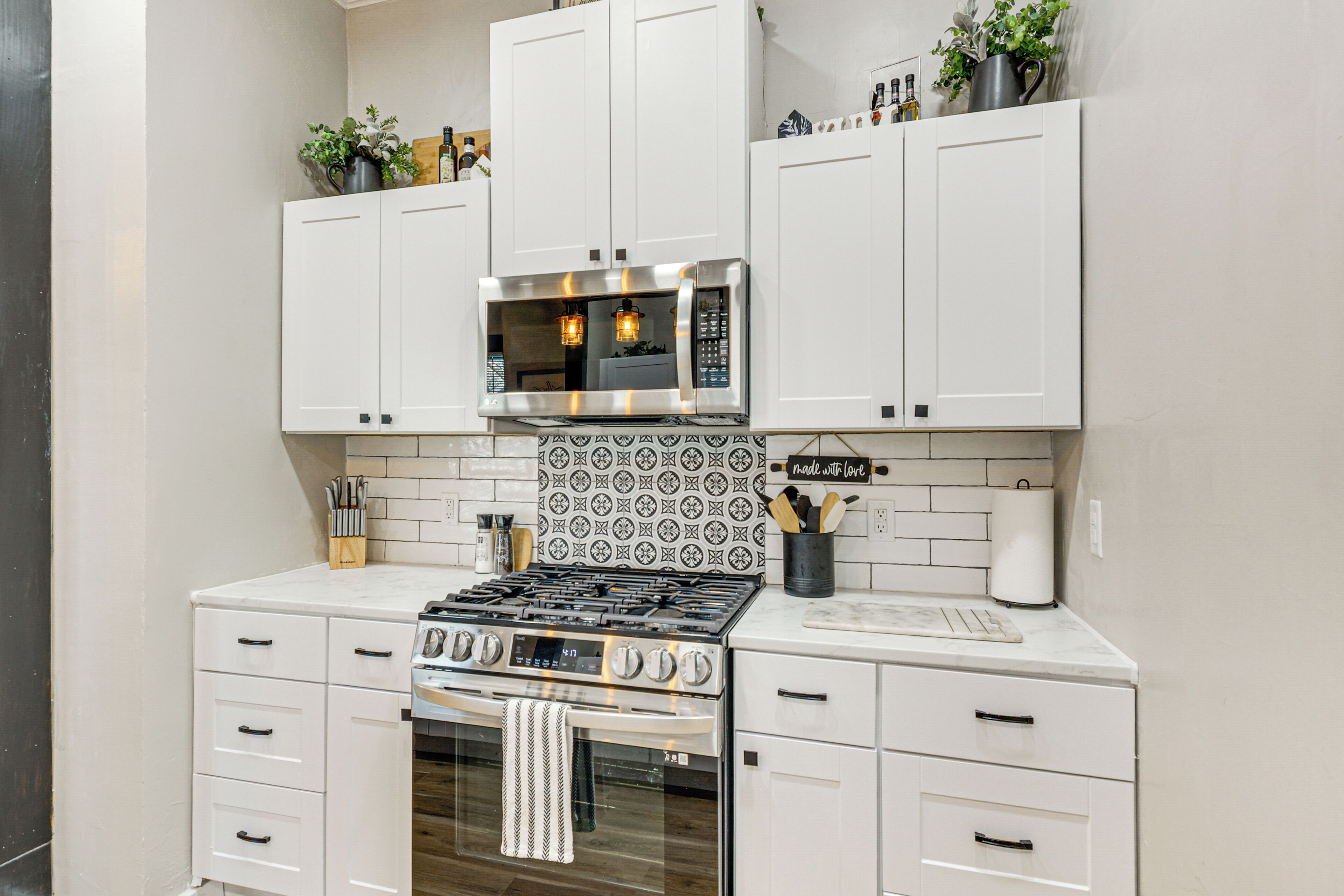 Cocina compacta con muebles blancos, estufa de acero inoxidable, microondas y salpicadero de azulejos.