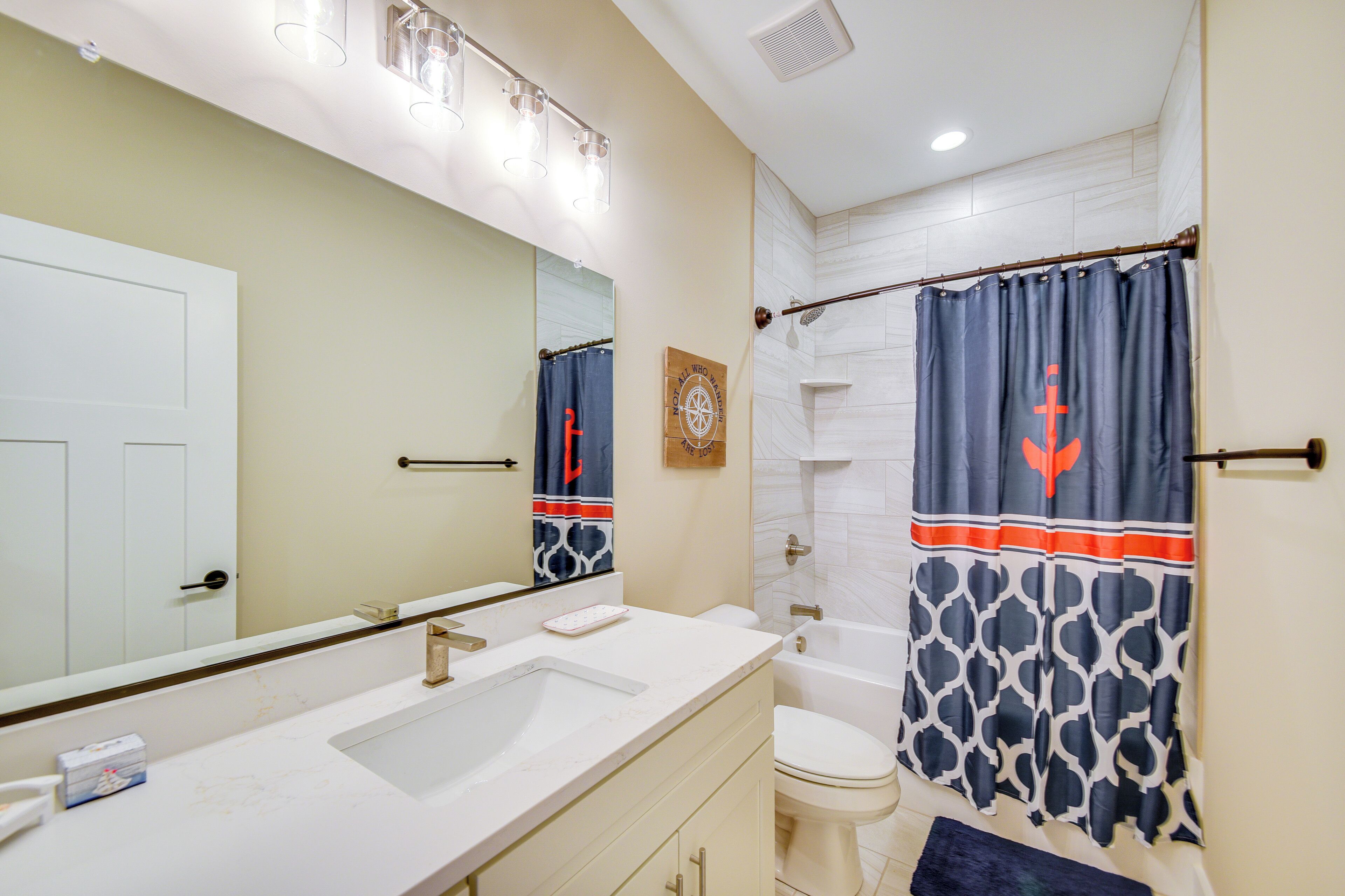 A bathroom with a white sink, mirror, and toilet. There is a shower curtain with a geometric pattern and a towel rack.