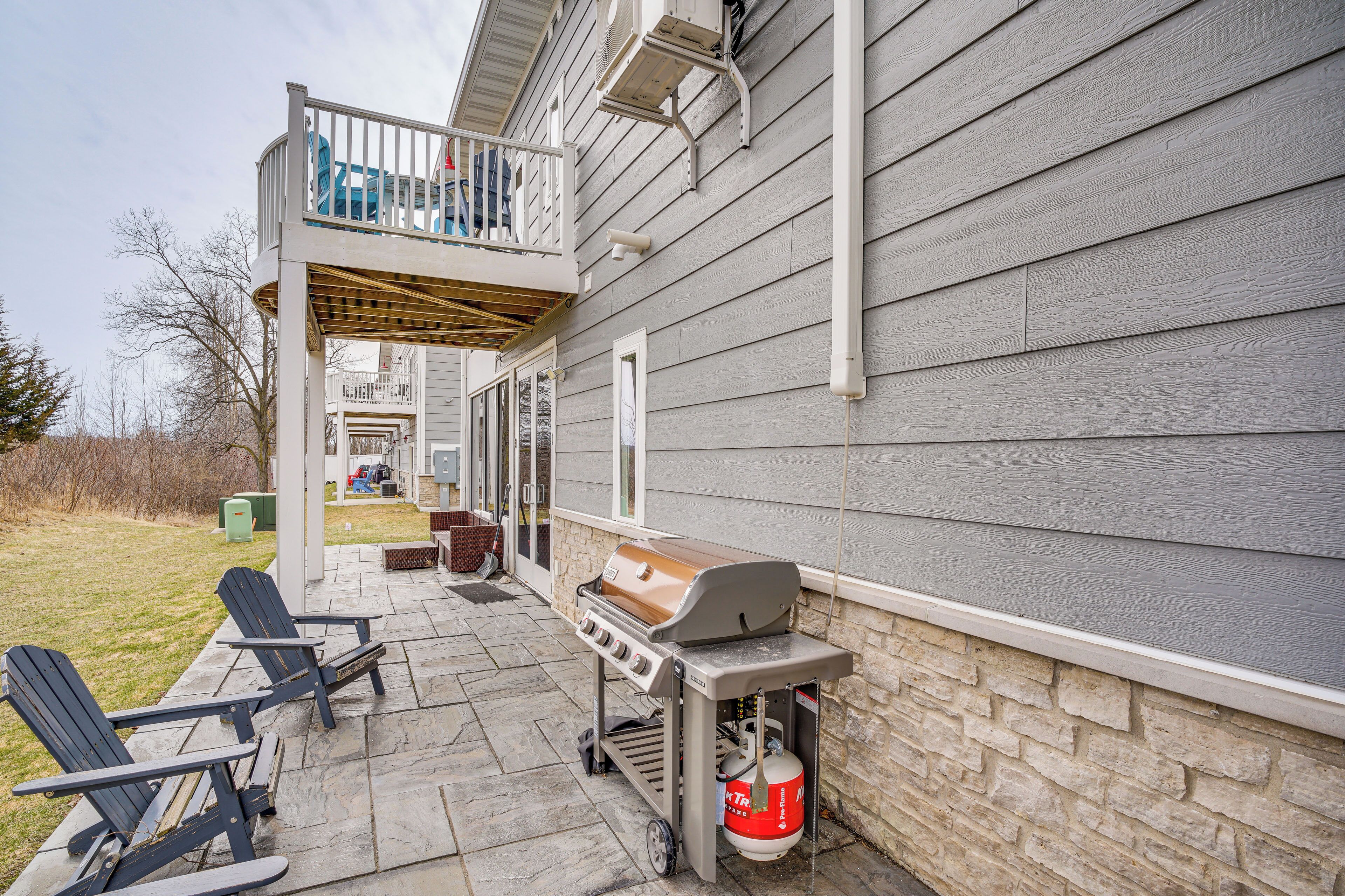 Une terrasse extérieure avec un barbecue, deux fauteuils Adirondack et un mur en pierre.