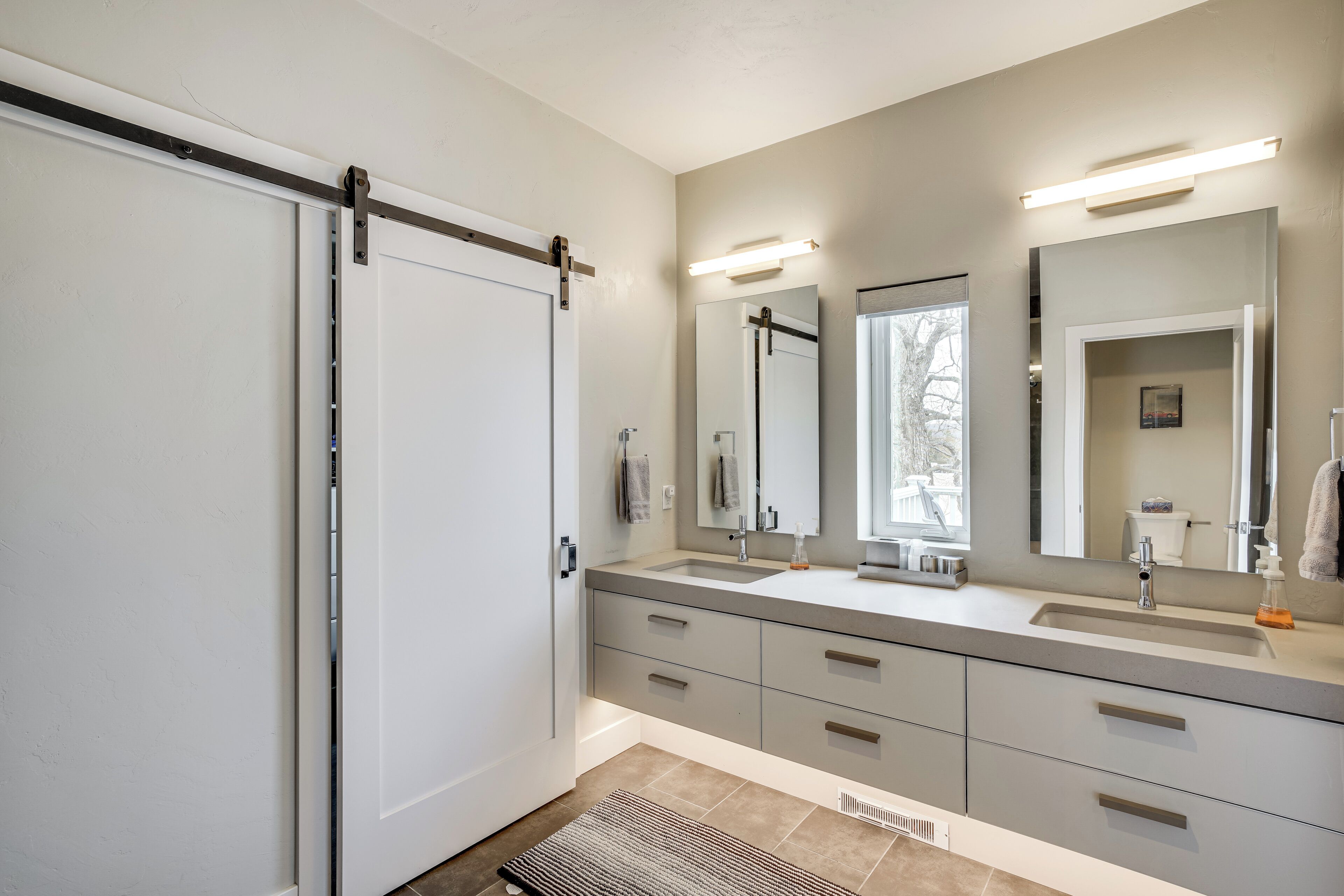 A modern bathroom with a large mirror, two sinks, and a sliding door.
