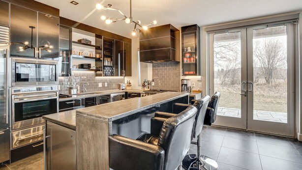 Una cocina moderna con electrodomésticos de acero inoxidable, una isla central con asientos tipo barra y un amplio ventanal corredero al exterior.