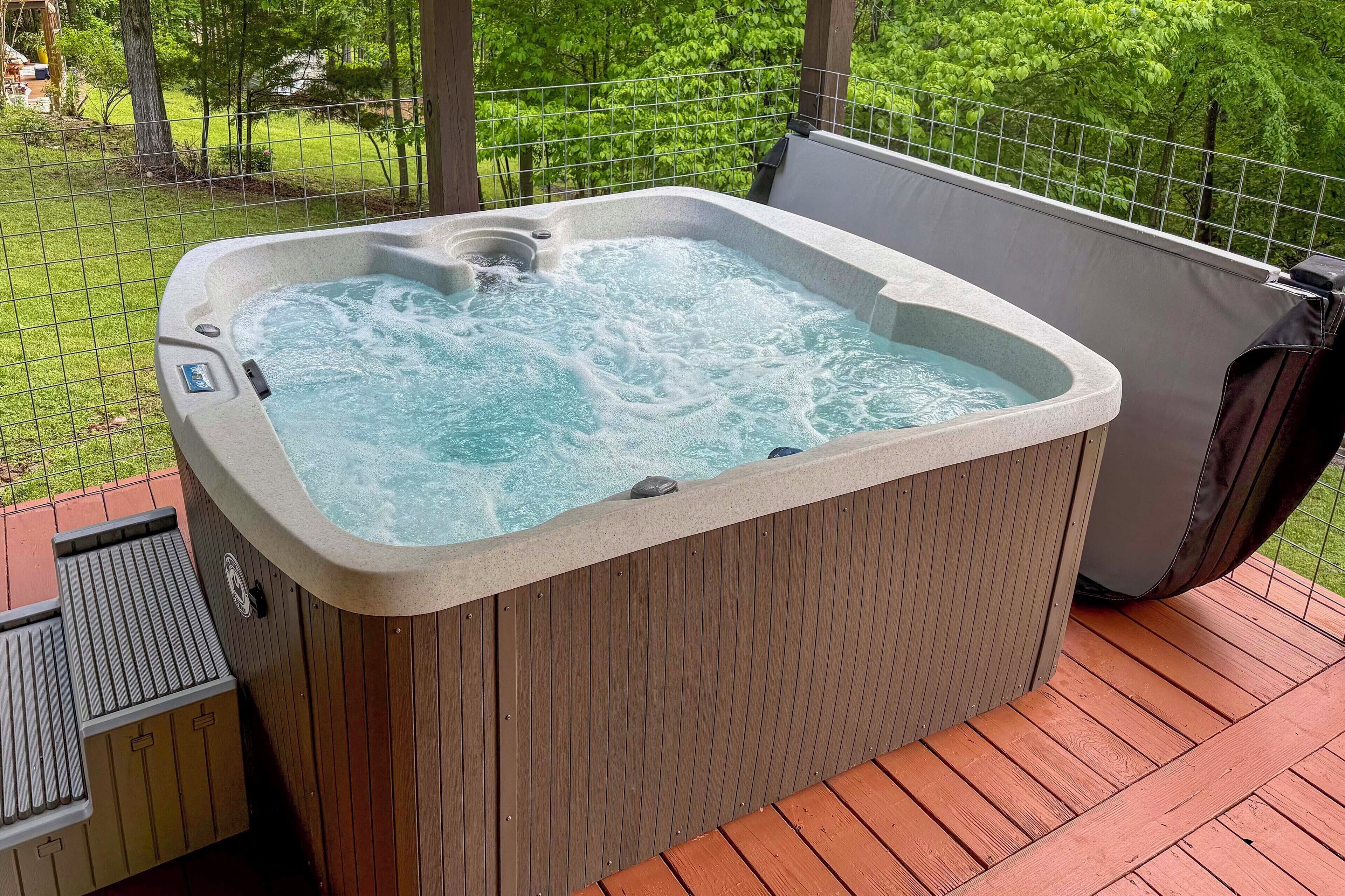 A hot tub on a wooden deck with a metal fence and greenery in the background.