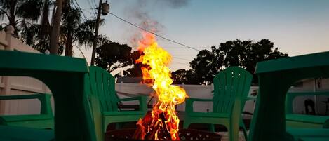 A fire burning in a metal container surrounded by green plastic chairs.