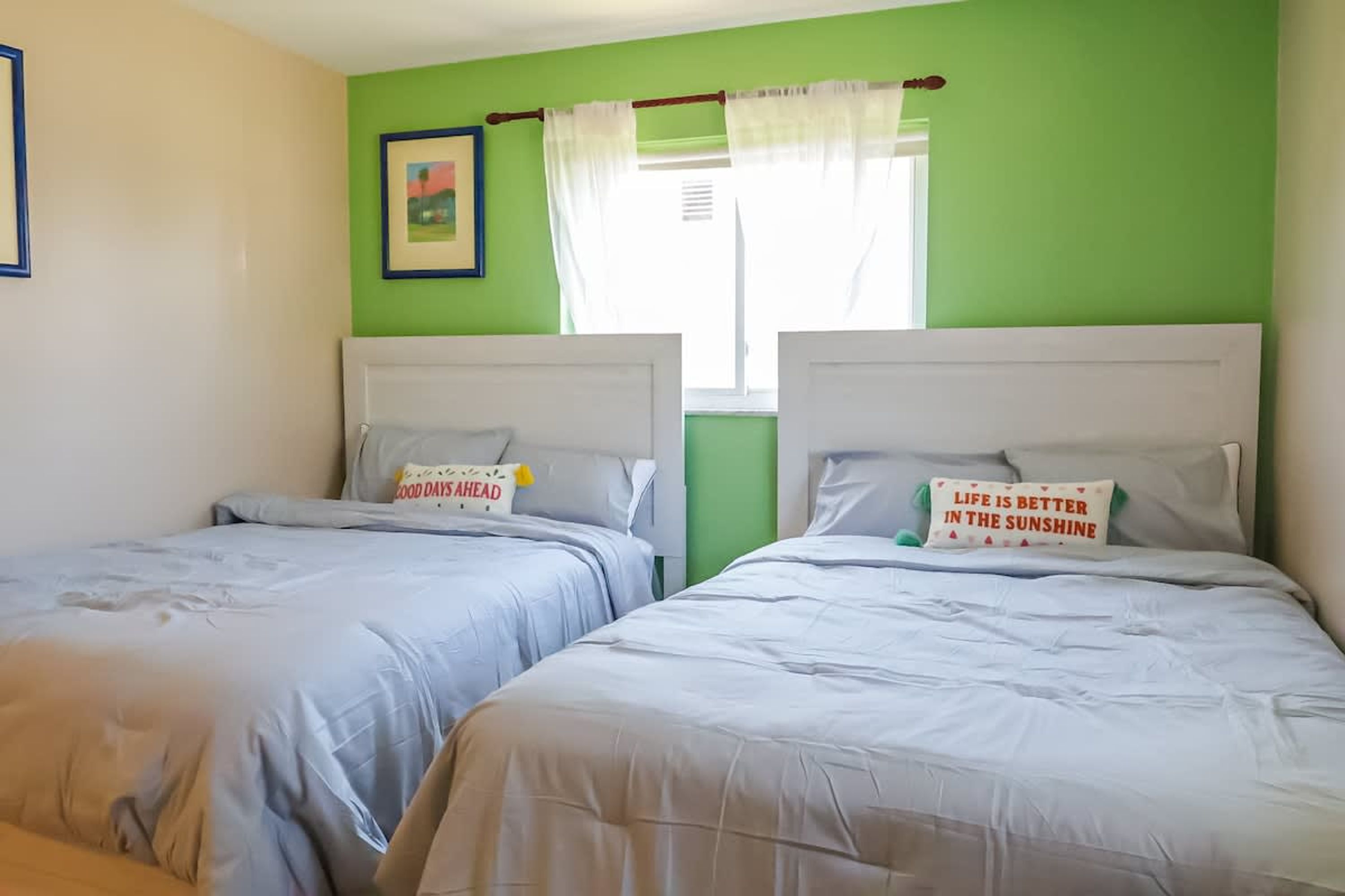 Een kamer met twee bedden, elk met een witte hoofdbord en een kussen met een bemoedigende quote.