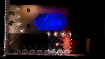Un área de piscina con una fuente de agua azul, rodeada de muros con luces decorativas y palmeras.