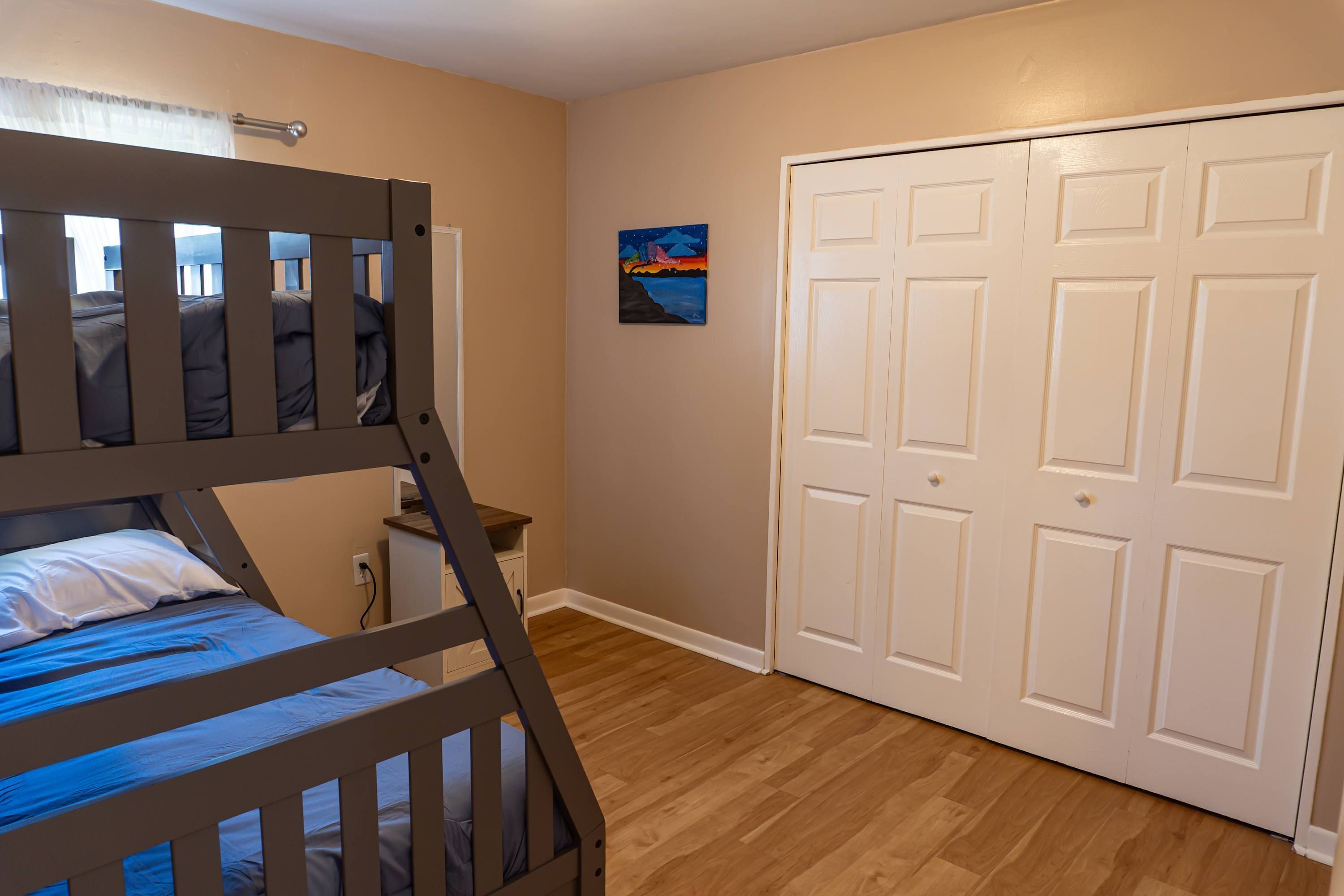 A bedroom with a bunk bed, a white door, and a painting on the wall.