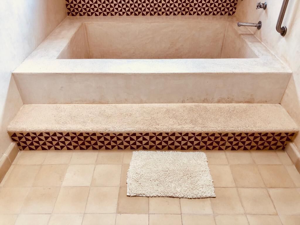 Une baignoire posée sur un sol carrelé de couleur beige, avec une bordure décorative.