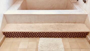 A bathtub with a beige tiled floor and a patterned border.
