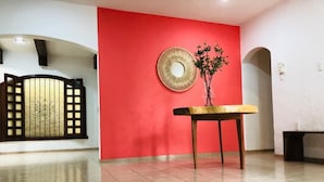 Una habitación amplia con una pared de acento roja, un espejo decorativo y una pequeña mesa con un florero.
