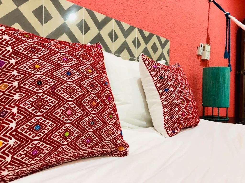 Een bed met opvallende kussens en een geometrisch patroon op de muur.