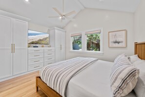 A bedroom with a bed, a wardrobe, a ceiling fan, and a window with a view of a beach. - Kiawah Exclusives | 459 Oceanwoods Cottage (Kiawah Island)