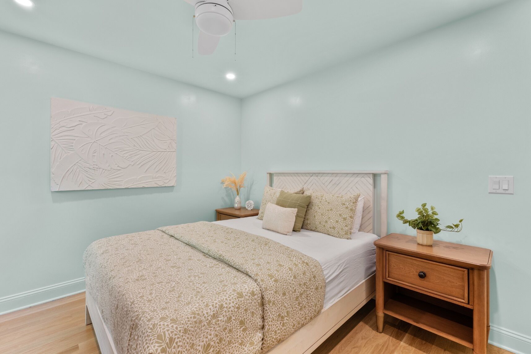 A bedroom with a bed, nightstands, a ceiling fan, a wall art piece, and a potted plant.