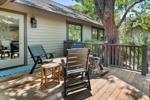 Une terrasse en bois avec des meubles d’extérieur, une porte d’entrée en verre et un arbre.