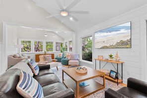 Un salon moderne doté d’une grande fenêtre, d’un ventilateur de plafond et offrant une vue sur la plage.