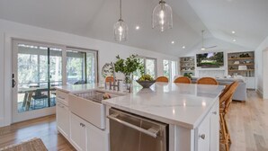 A modern kitchen with a large island, pendant lights, and a view to the outdoors.