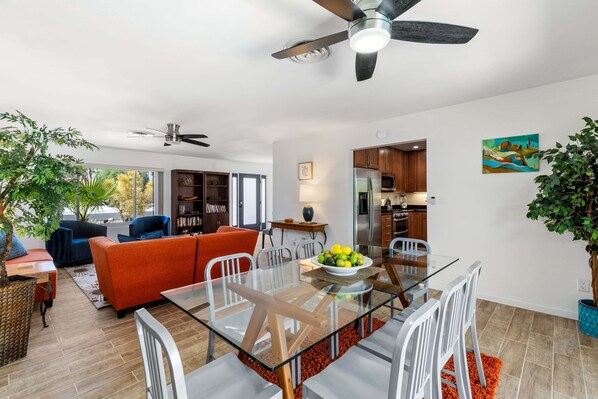 Uma sala de estar moderna com uma mesa de jantar de vidro, cadeiras brancas, um sofá vermelho e um ventilador de teto.