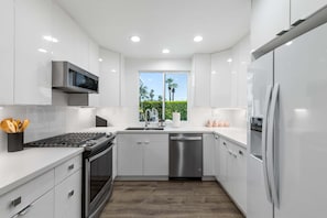 Una cocina moderna con armarios blancos, electrodomésticos de acero inoxidable y una ventana con vistas a palmeras.