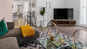 Ein modernes Wohnzimmer mit Sofa, Fernseher und Essbereich im Hintergrund.