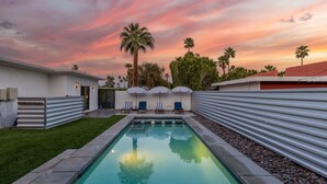 Ein Swimmingpool mit Liegestühlen und Sonnenschirmen, umgeben von Palmen und einem Sonnenuntergangshimmel.