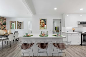 A modern kitchen with white cabinets, a central island with bar stools, and artwork on the walls.
