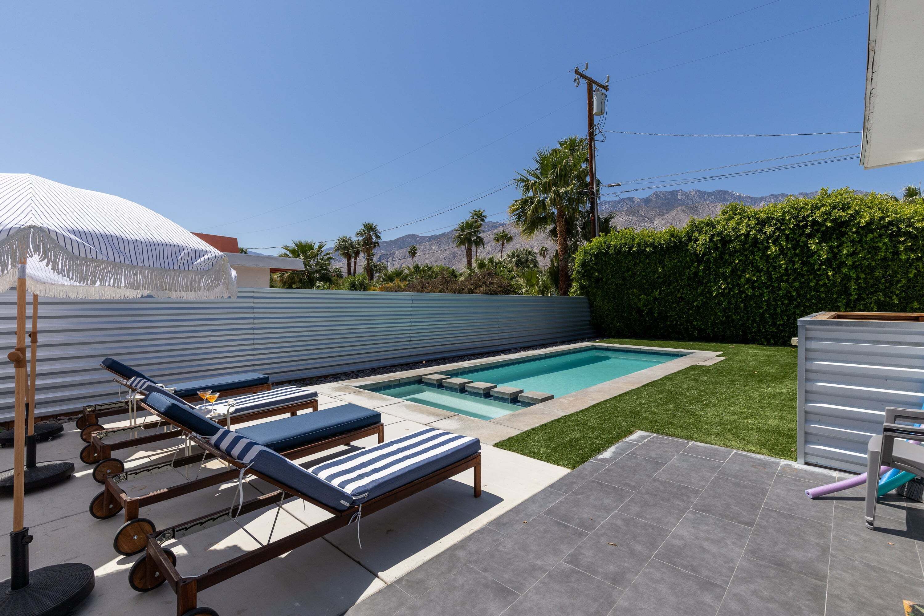 A backyard with a swimming pool, lounge chairs, and a hilly landscape in the background.