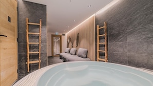 Une salle de spa équipée d’un bain à remous, de murs en bois et d’un canapé avec des coussins.