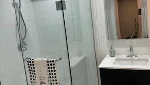 Un baño moderno con ducha envuelta en vidrio, un lavabo blanco y un mueble oscuro.