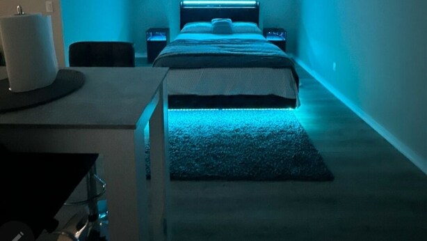 Un dormitorio con cama, mesitas de noche, un escritorio con computadora y una ventana pequeña.