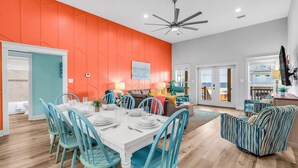 A dining area with a white table and blue chairs, a ceiling fan, and a bright orange wall. - Gulf View Beach Retreat with Hot Tub (Gulf Shores)