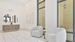 A modern hotel lobby with marble flooring, a grey sofa, a wooden cabinet, and artwork on the walls. - Luxurious Top Floor unit at The Residence at Coconut Point (Estero)