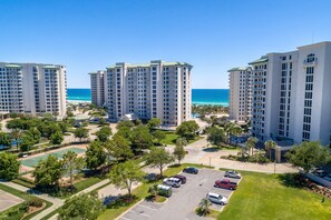 A high-rise residential building complex with multiple floors, a parking area, and a view of the ocean.