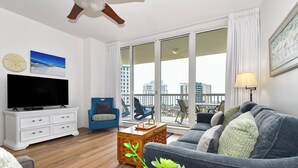 A modern living room with a flat-screen TV, a blue armchair, a grey sofa, and a wooden coffee table. - 7th Floor Beachfront Condo w/ Beachside Bar & Resort Pool in Destin! 🐚💙🌴 (Destin)