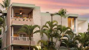 A multi-story hotel with balconies, palm trees, and a sunset sky.