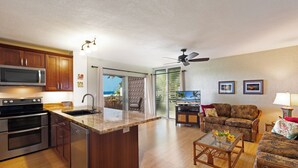 A modern kitchen with a microwave, oven, and dishwasher, a dining area with a table and chairs, and a living room with a sofa and a ceiling fan.
