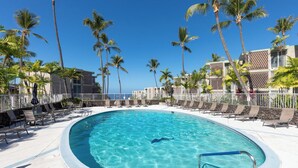 A pool surrounded by palm trees and lounge chairs, with a clear blue sky above.
