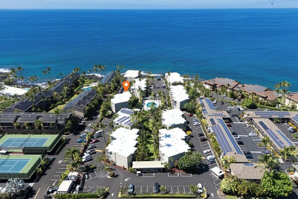 Vista aérea de un hotel costero con varias canchas de tenis, paneles solares y un estacionamiento.