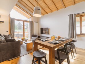 A modern dining area with a wooden table set for four, a sofa, and a TV on the wall.