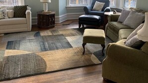 A living room with a light blue wall, a wooden floor, and a large window. There are two sofas, a coffee table, and a rug.