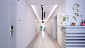 Een moderne hotelgang met een marmeren vloer, een receptiebalie met plantenbakken en een plafond met inbouwverlichting.