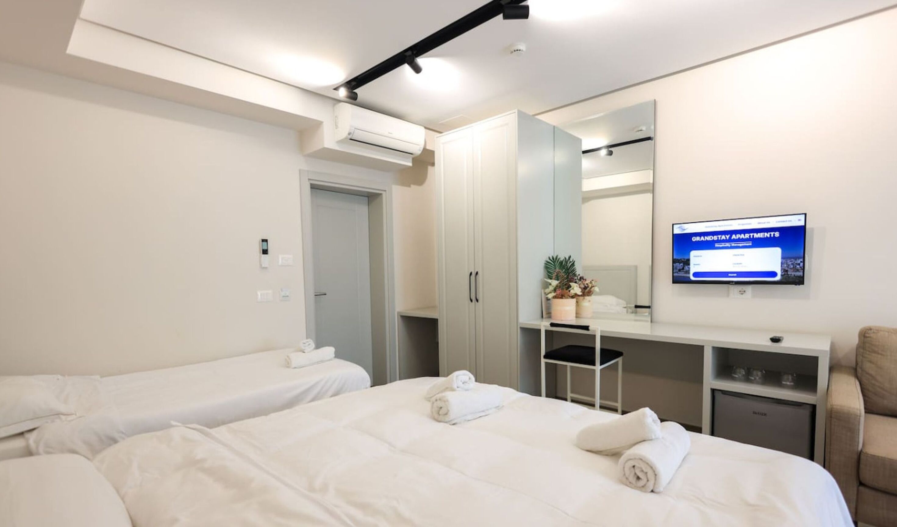 A hotel room with two beds, a desk, a chair, a TV, and a wardrobe.