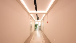 Een moderne hotelgang met een marmeren vloer, inbouwverlichting en een potplant.