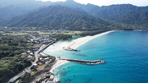 An aerial view of a coastal area with a beach, a rocky breakwater, and a residential area with houses and a road.