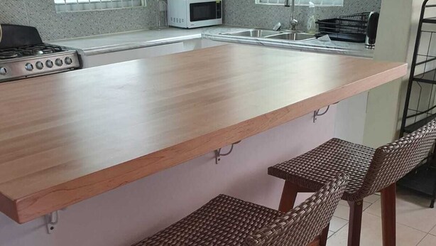A kitchen with a wooden island, two wicker bar stools, a microwave, and a gas stove. - Charming 3-bedroom bungalow with WiFi, AC in delightful Roseau (Roseau)