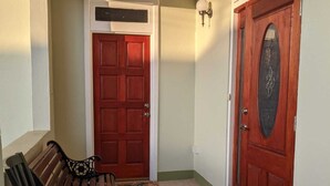 A wooden bench, a red door, and a white door in a hallway. - Charming 3-bedroom bungalow with WiFi, AC in delightful Roseau (Roseau)