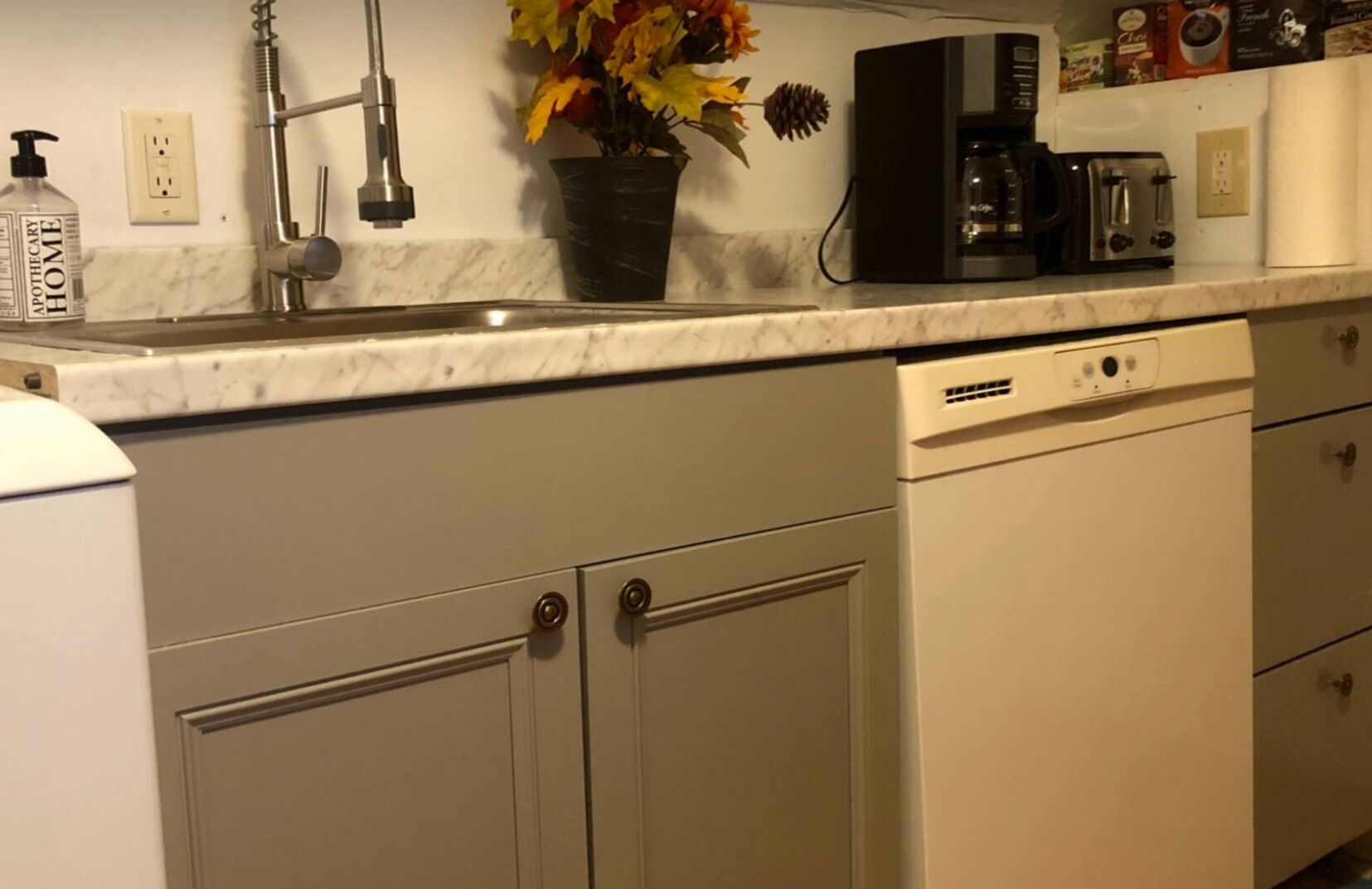 A kitchen with a sink, a coffee maker, a toaster, and a dishwasher.