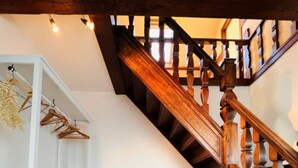 A staircase with wooden balusters and a white wall with a wicker chair and shelves. - Holiday Home in Wenduine Near Zeedijk (De Haan)