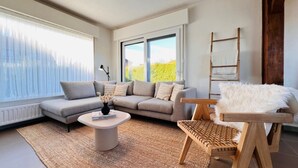 A modern living room with a grey sofa, a round coffee table, and a wooden chair with a white furry throw. - Holiday Home in Wenduine Near Zeedijk (De Haan)