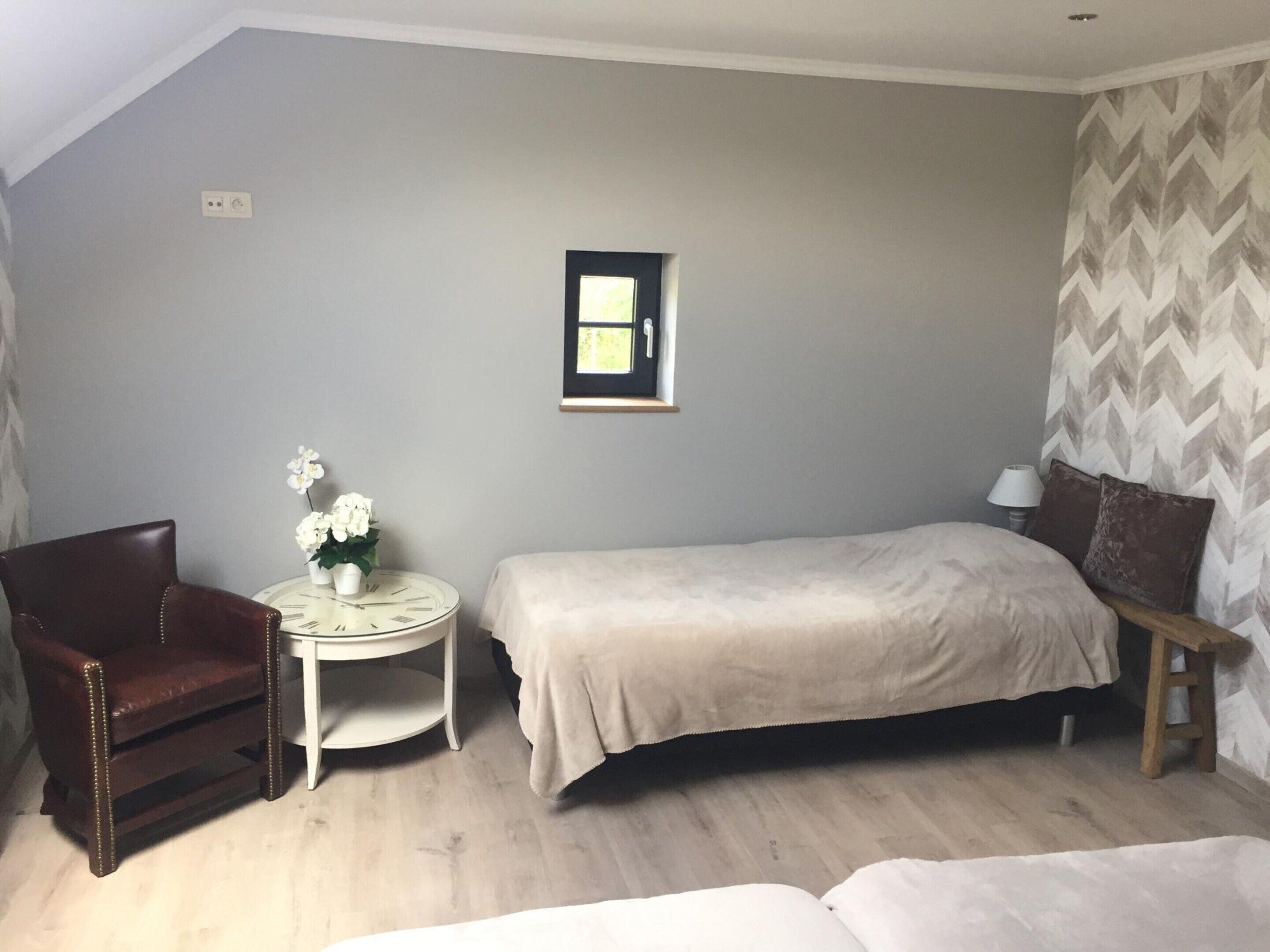 Une petite chambre à coucher, bien rangée, avec un lit simple, une chaise, une petite table ornée de fleurs et un tableau accroché au mur.