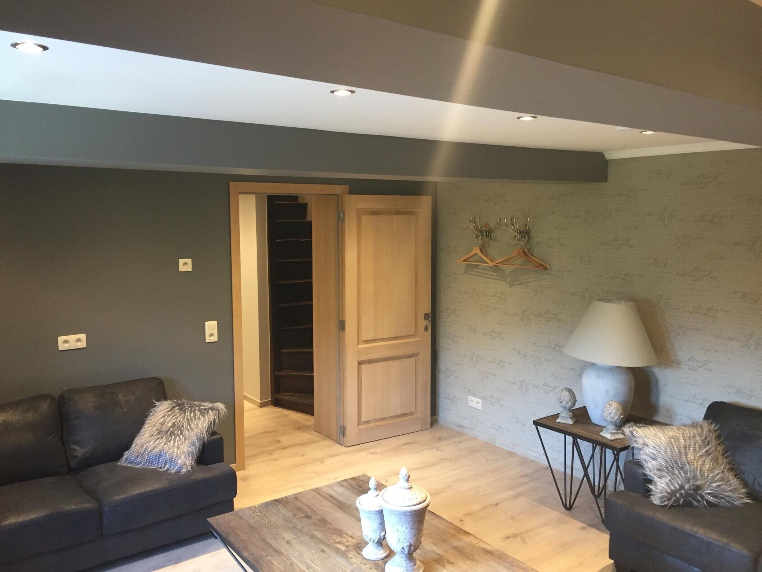 Un salon moderne avec deux canapés sombres, une table basse en bois et une porte donnant sur un escalier.