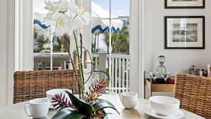 A dining area with wicker furniture, white tableware, and a view of the outdoors through large windows. - 30A Sunset Beach House - Villa Infinity (Panama City Beach)